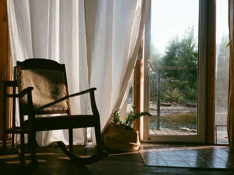 Rocking chair by the window of a river cabin at dusk, with soft natural lighting and a calm atmosphere.