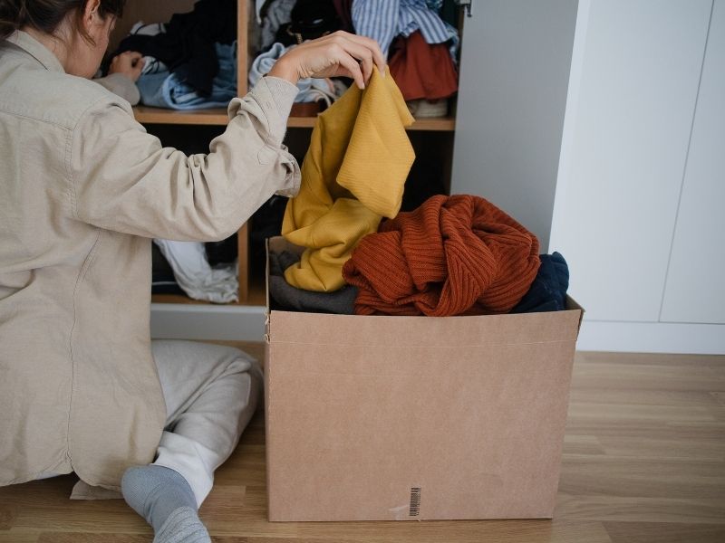Woman organizing and decluttering clothes from a closet for a clutter free home and heart.