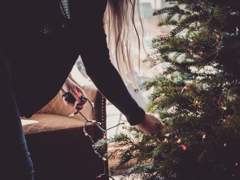 Woman decorating a Christmas tree indoors, symbolizing the creation of meaningful traditions during solitude.
