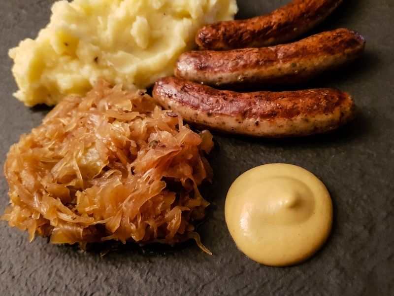 A plate of hearty Bratwurst with sauerkraut, and mash potatoes, showcasing simple winter food idea for comfort and warmth.