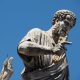 A close-up photograph of the majestic marble statue of Saint Peter in St. Peter's Square at the Vatican, clutching the keys of the kingdom of heaven in his right hand against a bright blue sky.